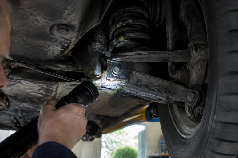 Inspection minutieuse du châssis et des longerons d'une BMW E30 pour évaluer la corrosion de la coque.