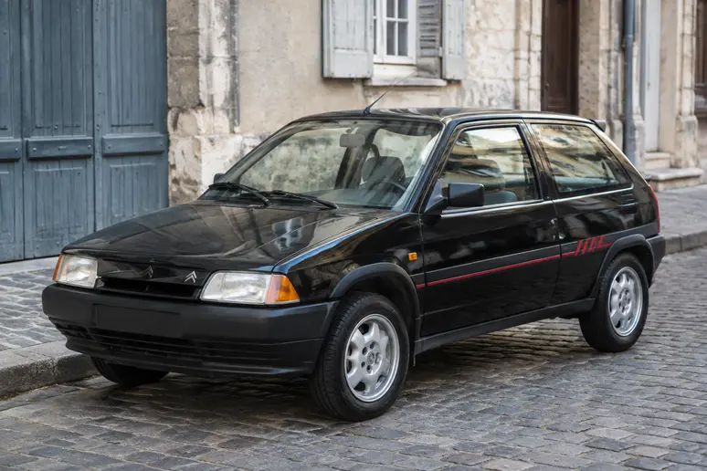 Une Citroën AX Sport stationnée dans une rue française montrant ses jantes d'origine