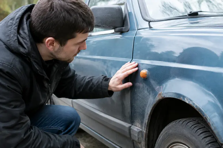 Un acheteur examine attentivement la carrosserie d'une citadine d'occasion avant l'achat.