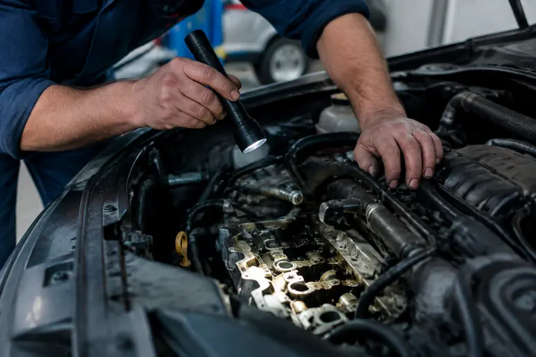 Mécano inspectant le bloc moteur d'une voiture lors d'un contrôle de fiabilité moteur puretech
