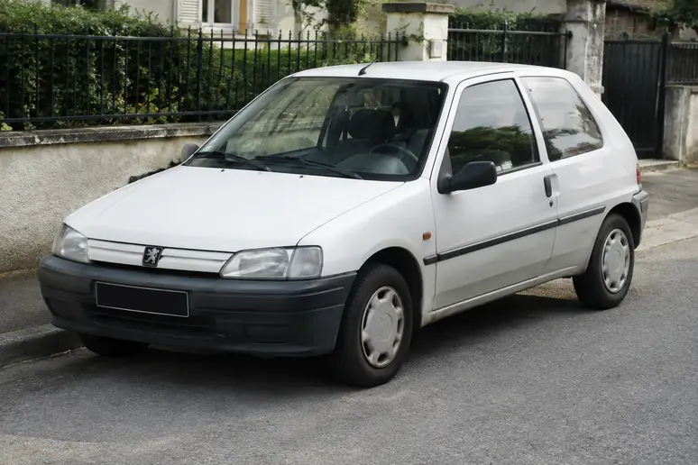 Une berline Peugeot 106 blanche stationnée dans une rue résidentielle pour illustrer la cote en occasion.