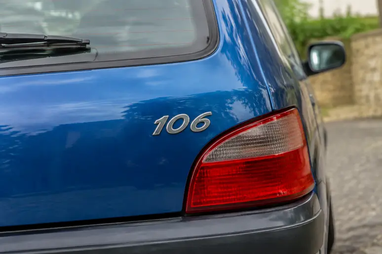 Gros plan sur le monogramme et l'état de conservation d'une Peugeot 106 de collection.