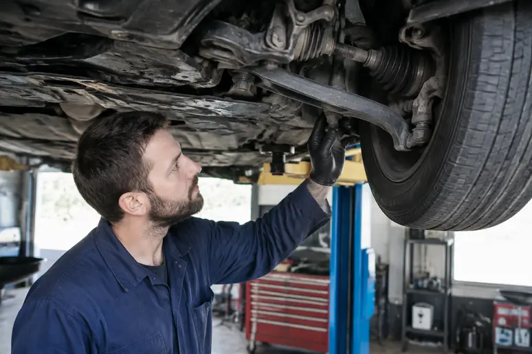 Mécanicien inspectant les triangles de suspension d'une Alfa Romeo 156 sur un pont élévateur.