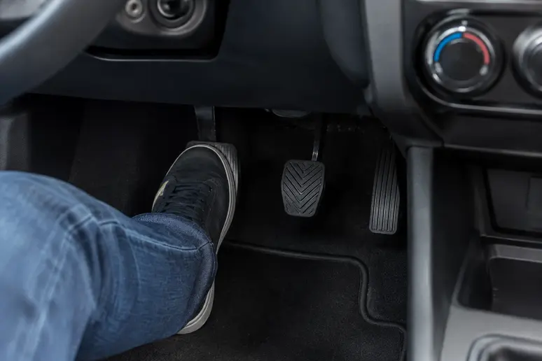 Pied du conducteur pressant la pédale d'embrayage dans l'habitacle d'une petite voiture