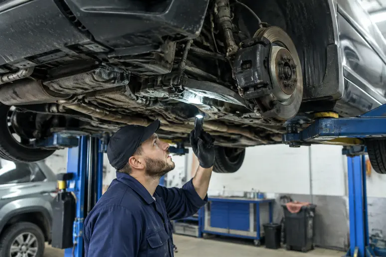 Vérification des dessous d'un Suzuki Vitara d'occasion sur un pont élévateur en atelier.